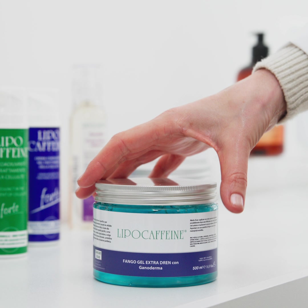 Una mano apre un vasetto di fango gel Lipocaffeine accanto ad altri prodotti della linea.